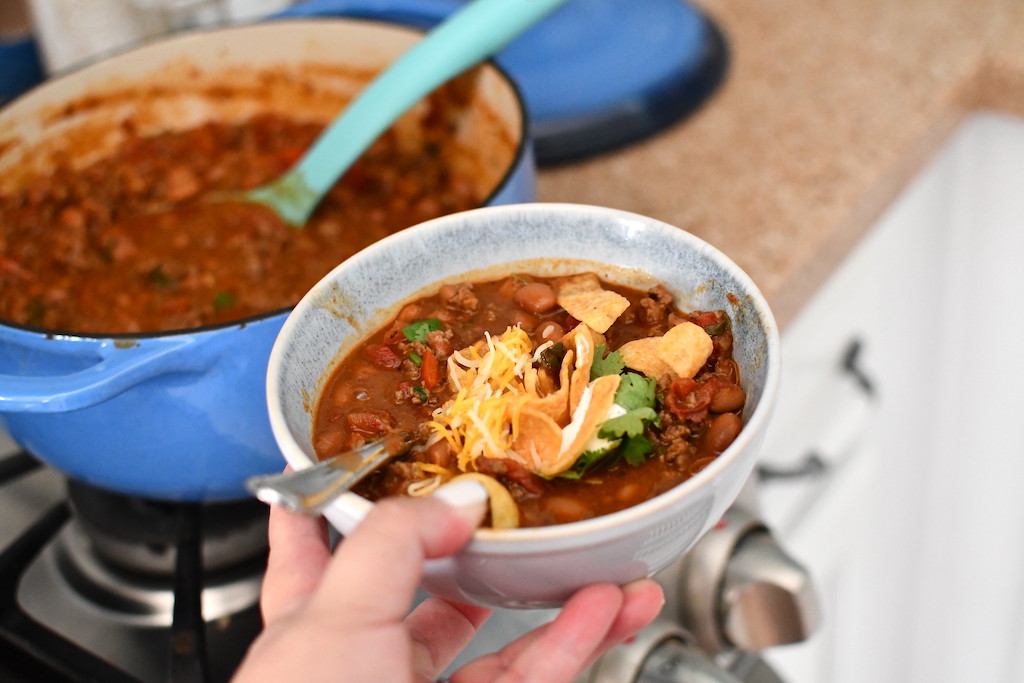 hand holding bowl of chili with pot in background 