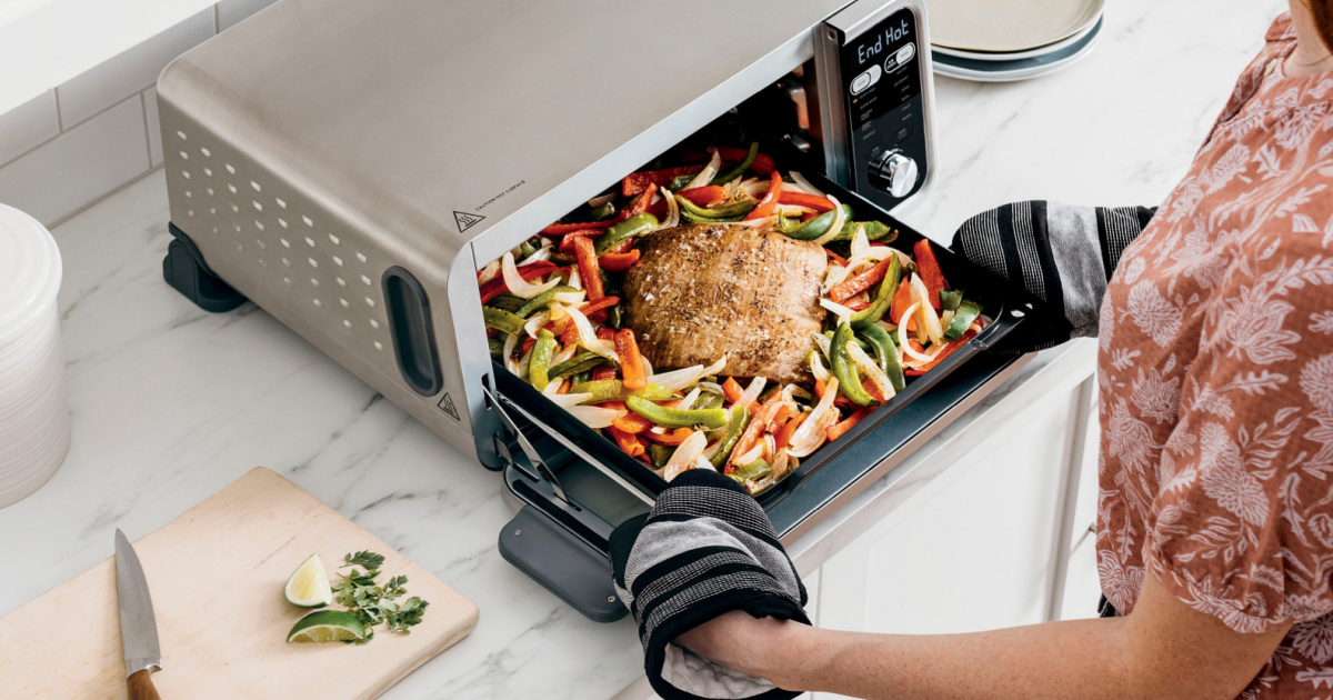woman putting a roast and vegetables in a ninja foodi air fryer toaster oven