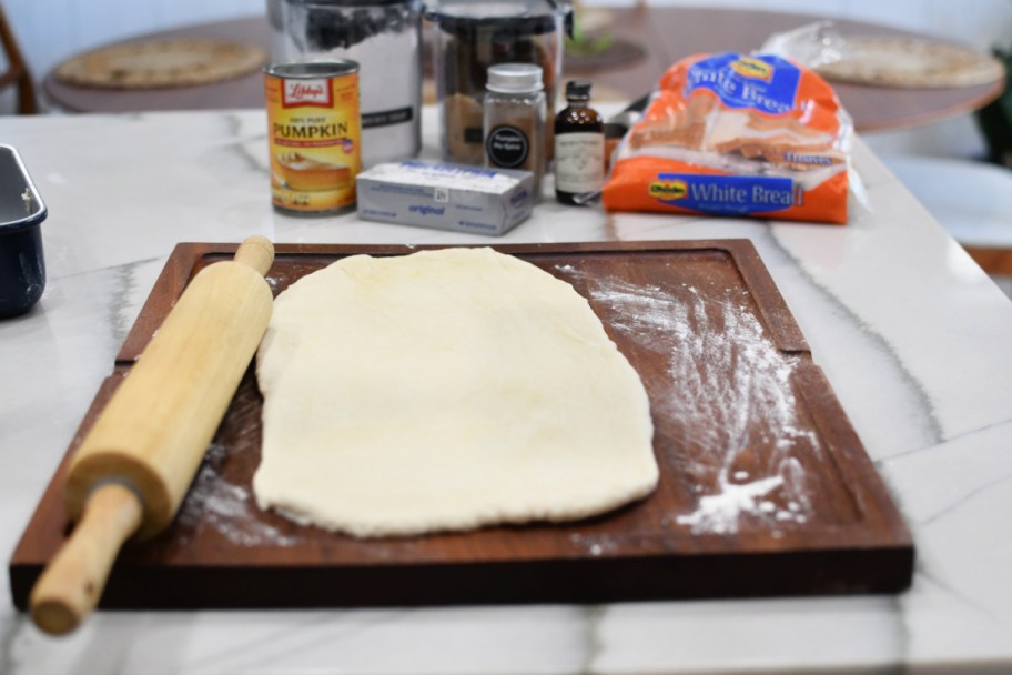 rolling bread dough with a rolling pin to make cinnamon rolls 