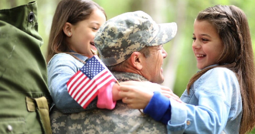 girls hugging a man in a military uniform