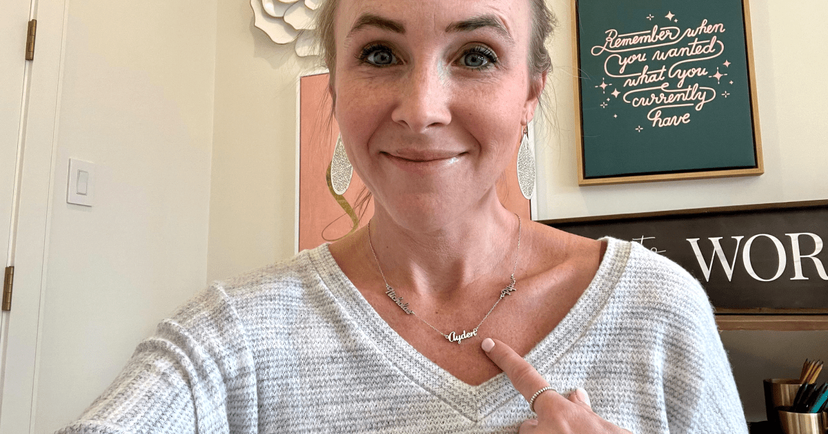 woman smiling and pointing at her name necklace 