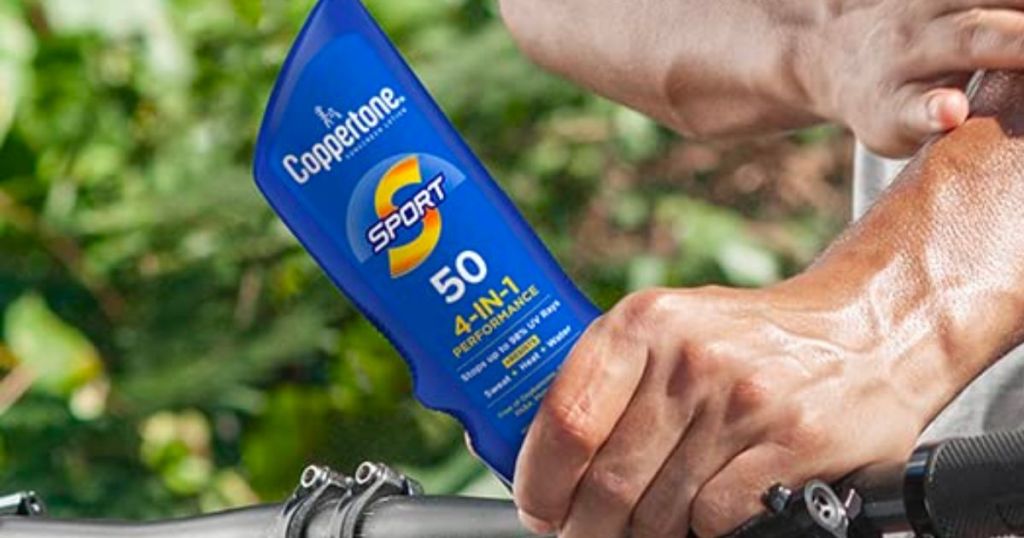 A man's hand holding a bottle of coppertone sport spf 50 4-in-1 lotion