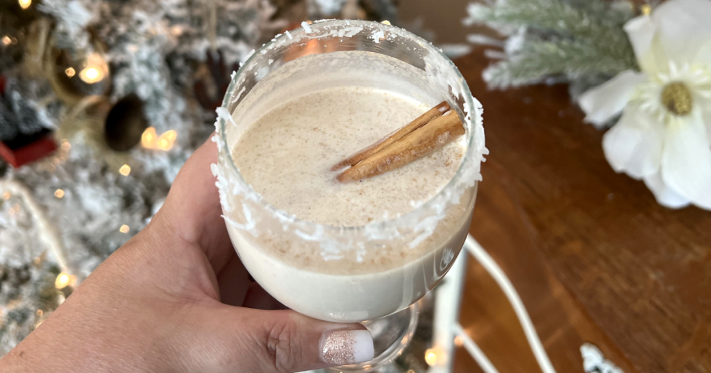 holding glass of Coquito with cinnamon stick
