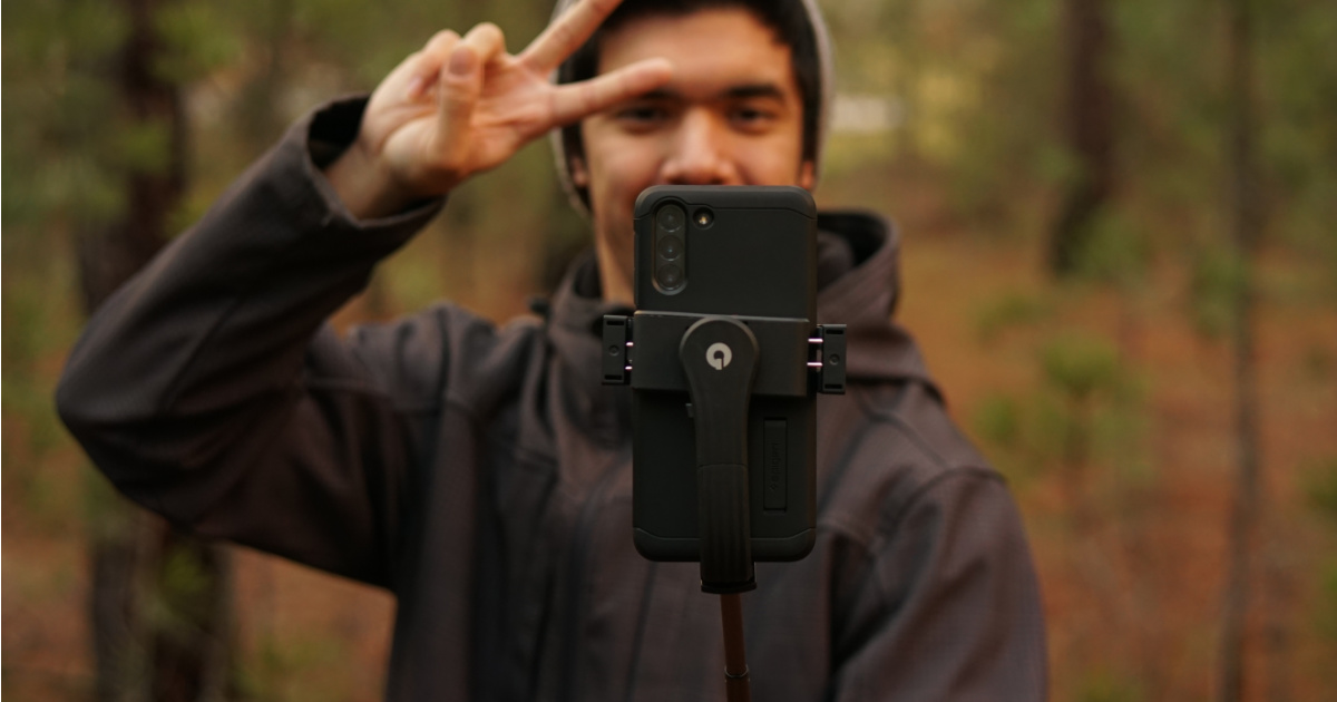 Man making peace sign with hand in front of a cell phone on a tripod