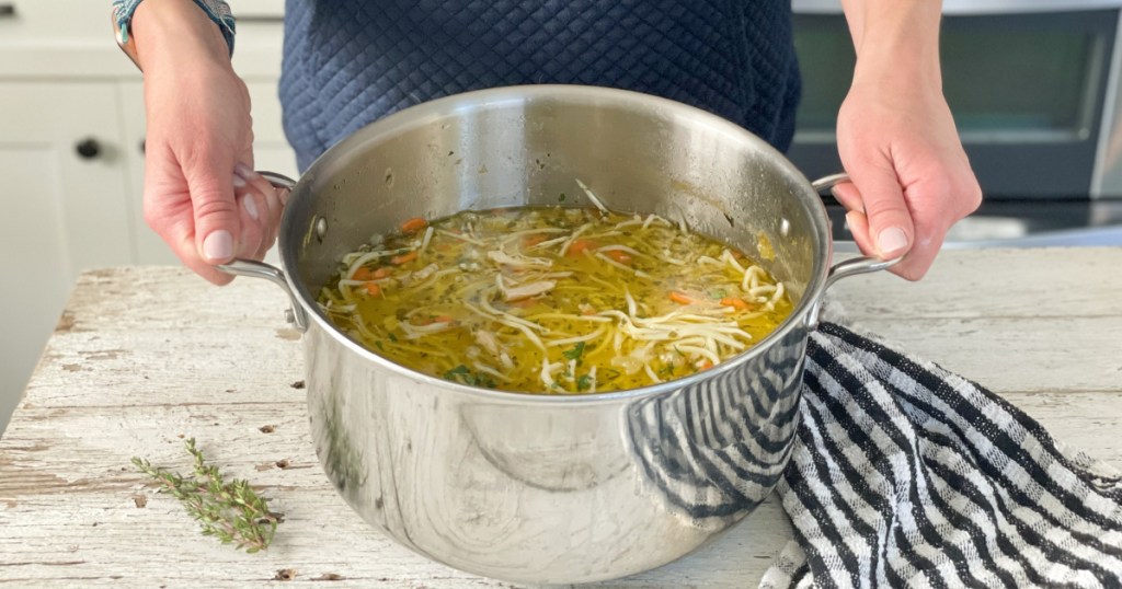 holding large pan with chicken noodle soup 