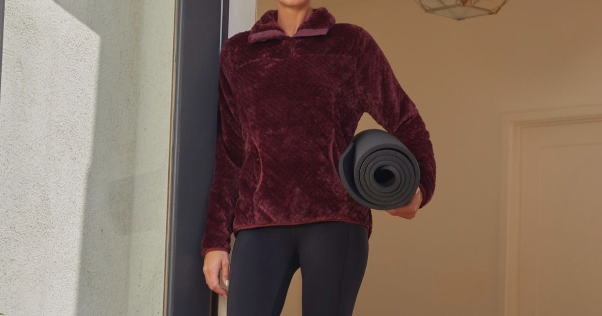 woman wearing a sherpa pullover with a rolled up yoga mat under her arm