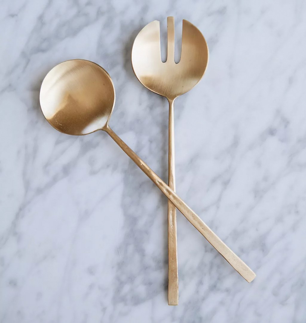 brass salad servers sitting on marble surface 