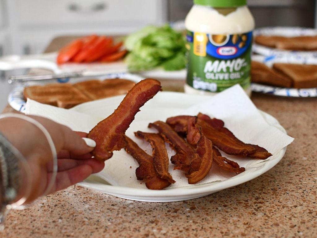 person taking piece of bacon from plate of bacon