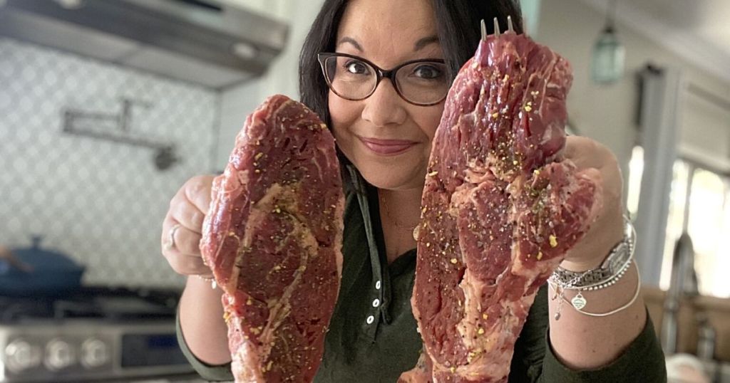 person holding 2 raw steaks up 