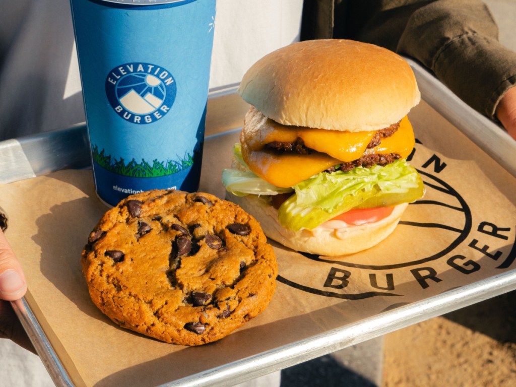 holding a tray with a burger, cookie, and fountain drink