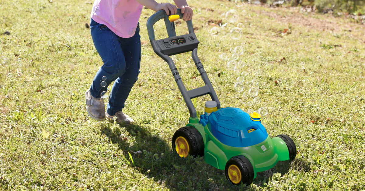 kid pushing a toy bubble mower on some green grass