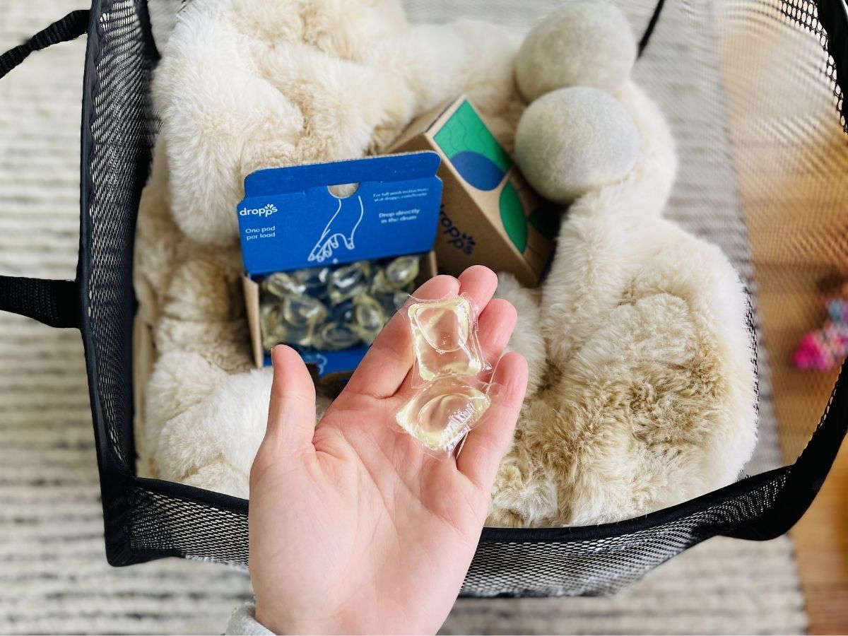 hand holding clear pods in palm over basket of laundry
