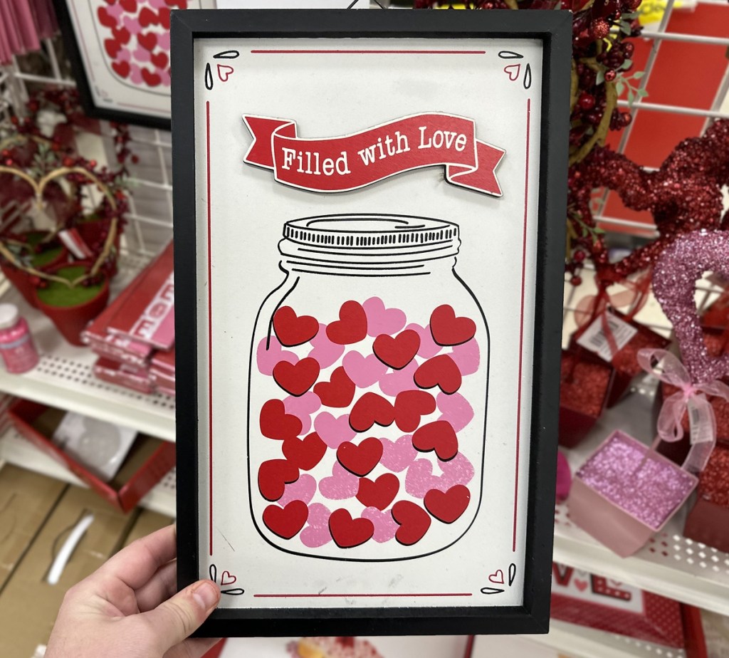 hand holding a sign that says "filled with love" with a jar filled with hearts