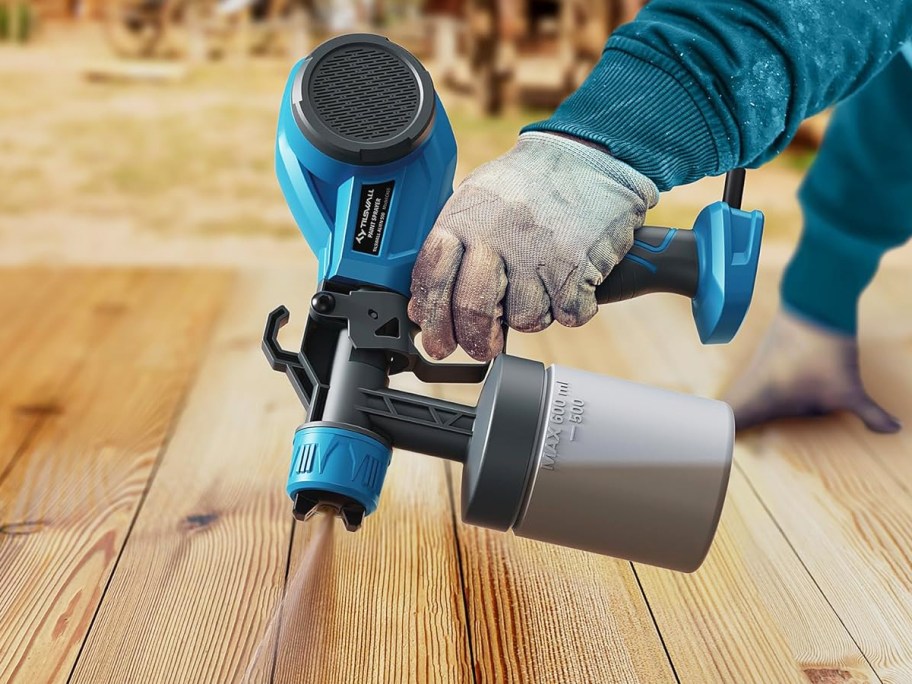 using a blue and black paint sprayer on a wood deck