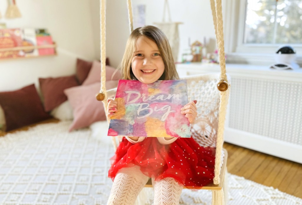 girl sitting on swing holding canvas painting