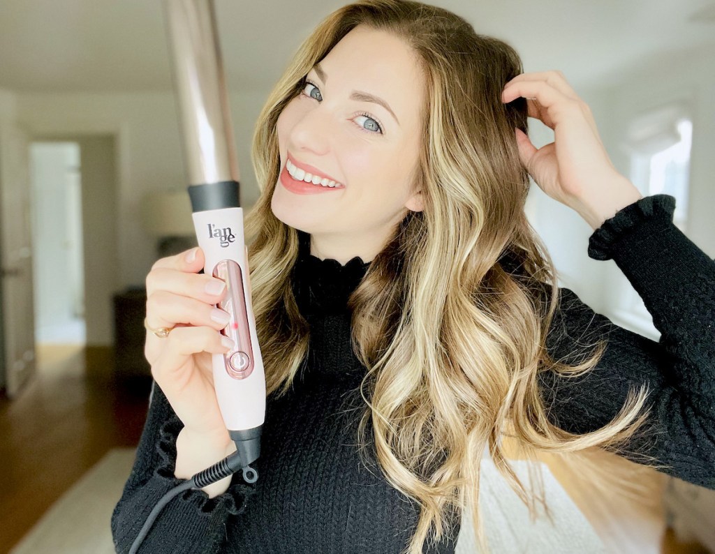 woman holding curled hair while holding pink lange hair curling wand