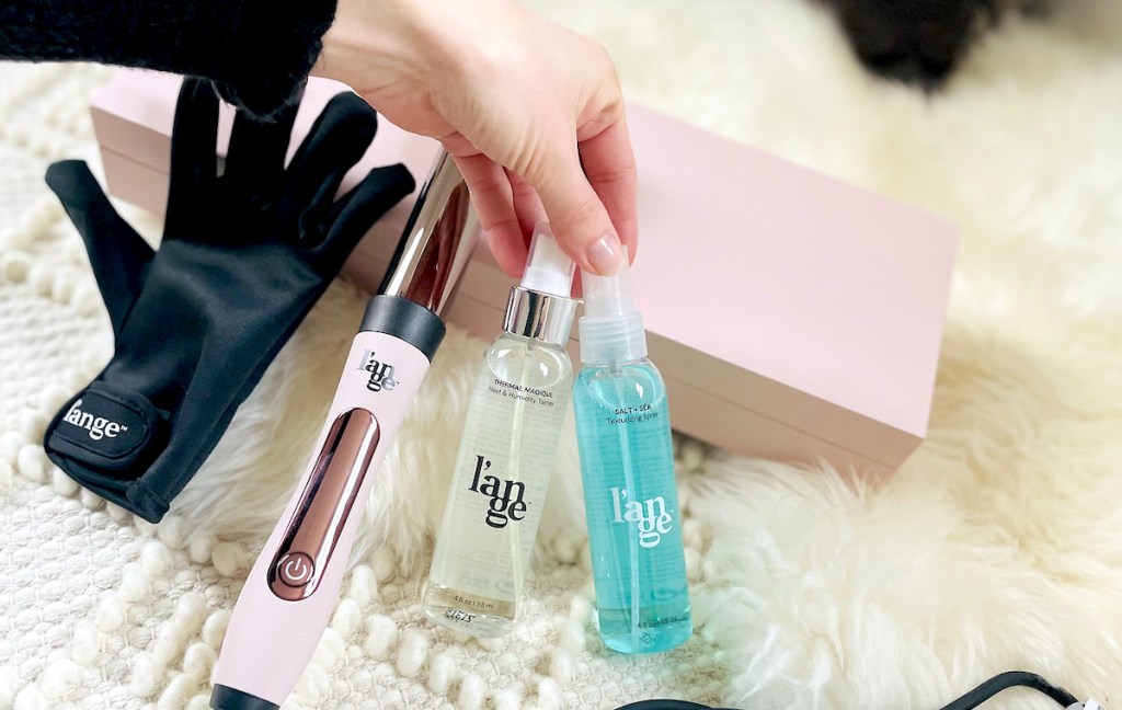 hand holding two bottles of hair products on white fur rug