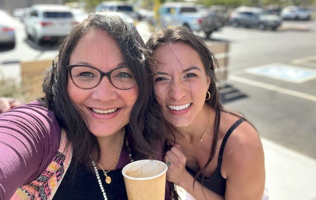 two dark haired woman standing outside taking selfie smiling