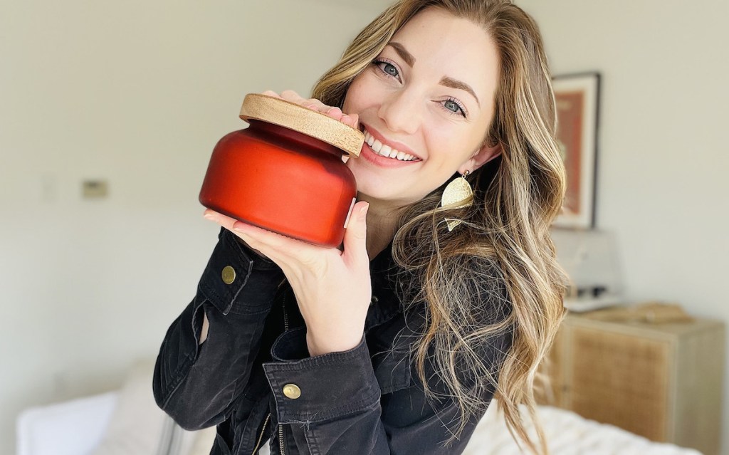 woman holding red volcano dupe candle next to face smiling