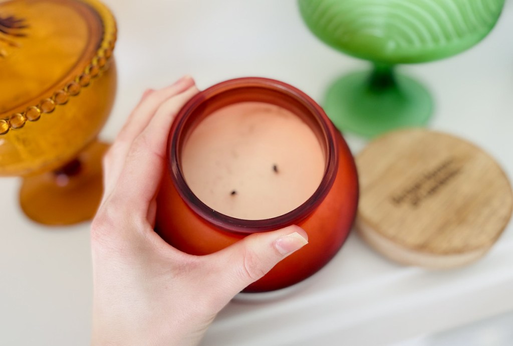 hand holding top of red glass jar candle