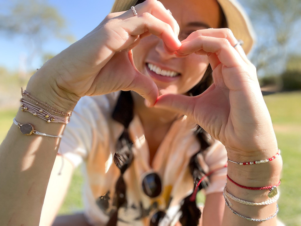 woman wearing Pura Vida jewelry making heart with hands 