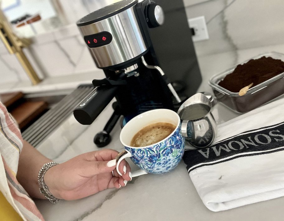 holding cup of coffee in front of espresso machine