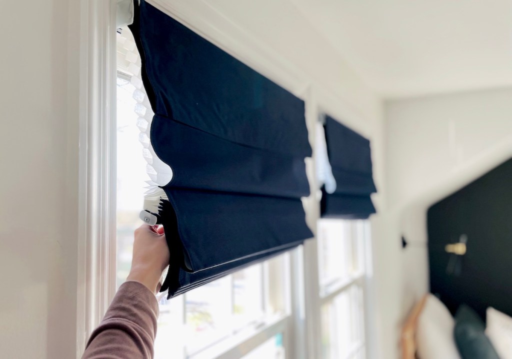 close up of hand pulling down corner of navy blue roman shades on window