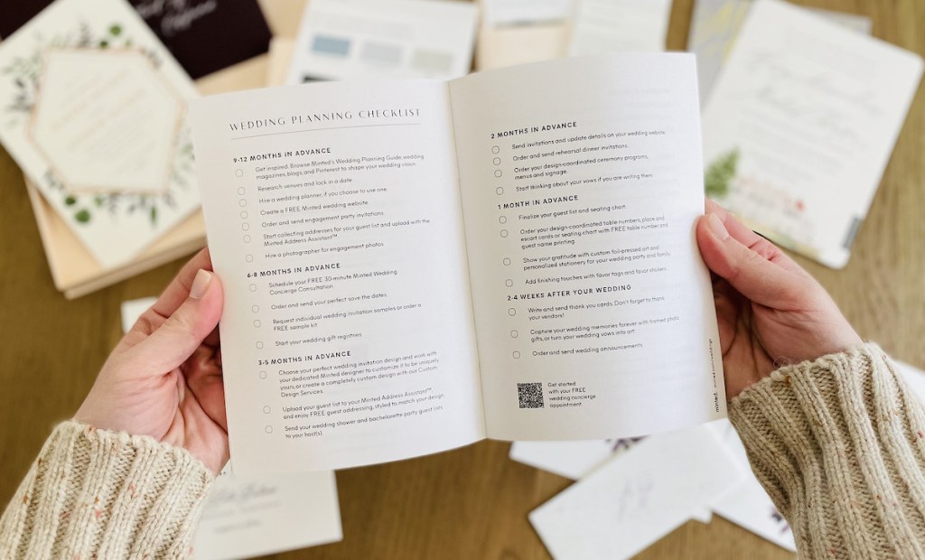 hands holding wedding checklist over table with stationery samples