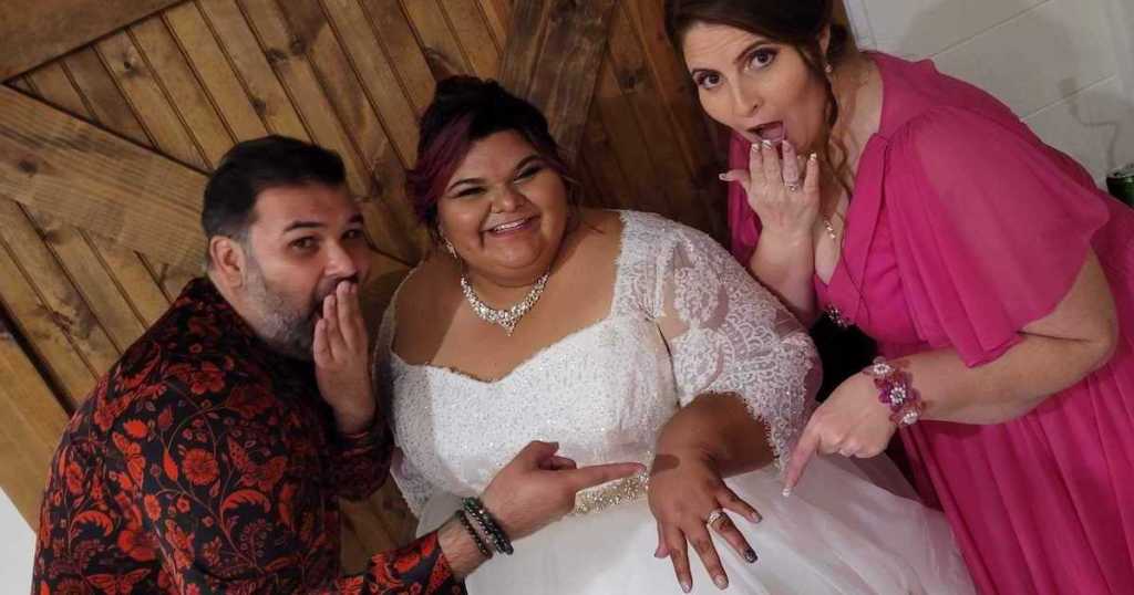 man and woman posing with bride showing off wedding ring