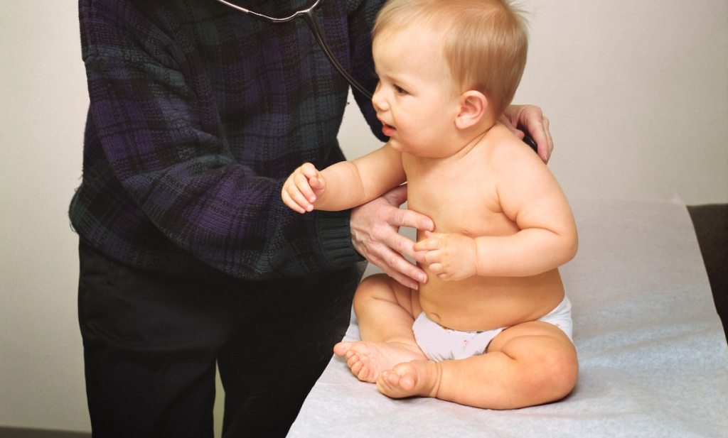 baby in diaper sitting on pediatrician table with doctor listening to breathing
