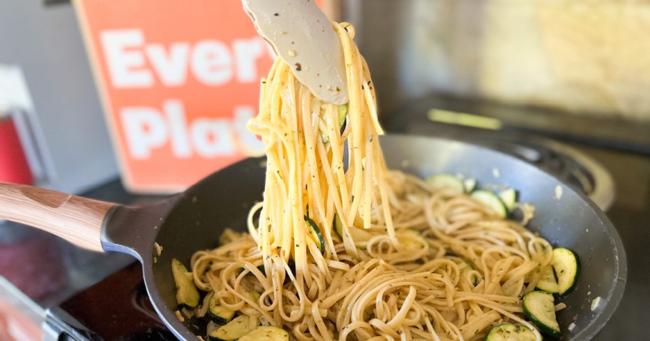 tongs pulling up pasta from a pan with an EveryPlate box pictured in the background