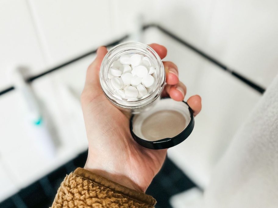 hand holding glass container of toothpaste tablets