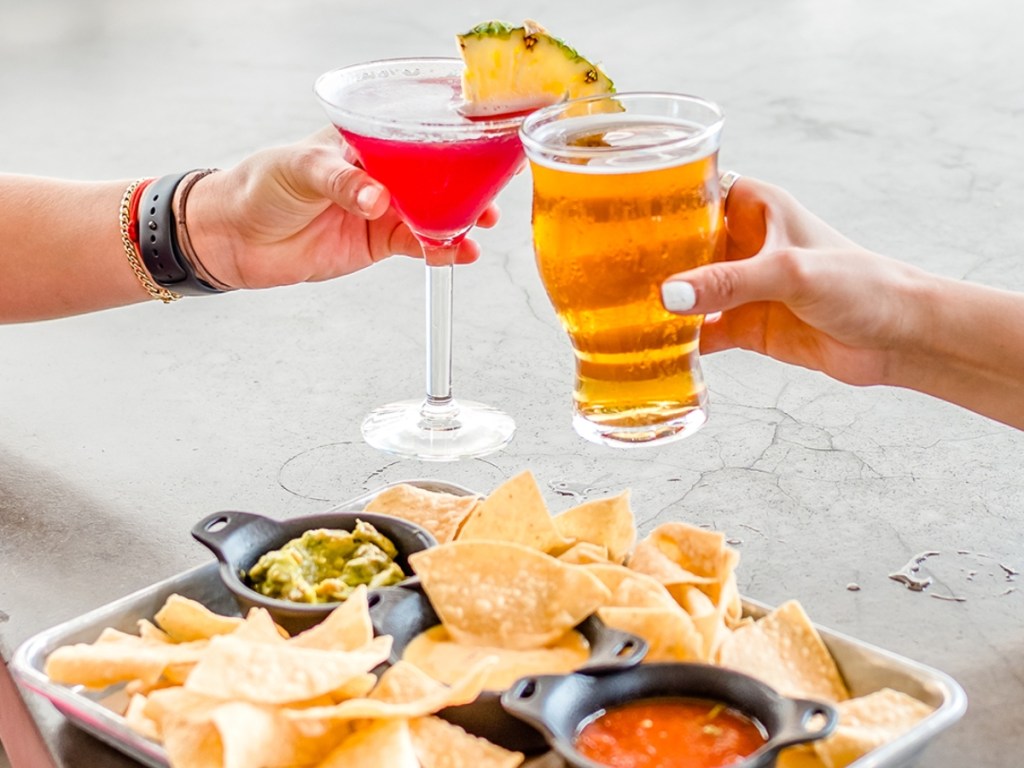 toasting 2 beverages over a plate of appetizers