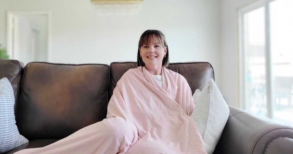 woman wrapped in pink blanket sitting on couch