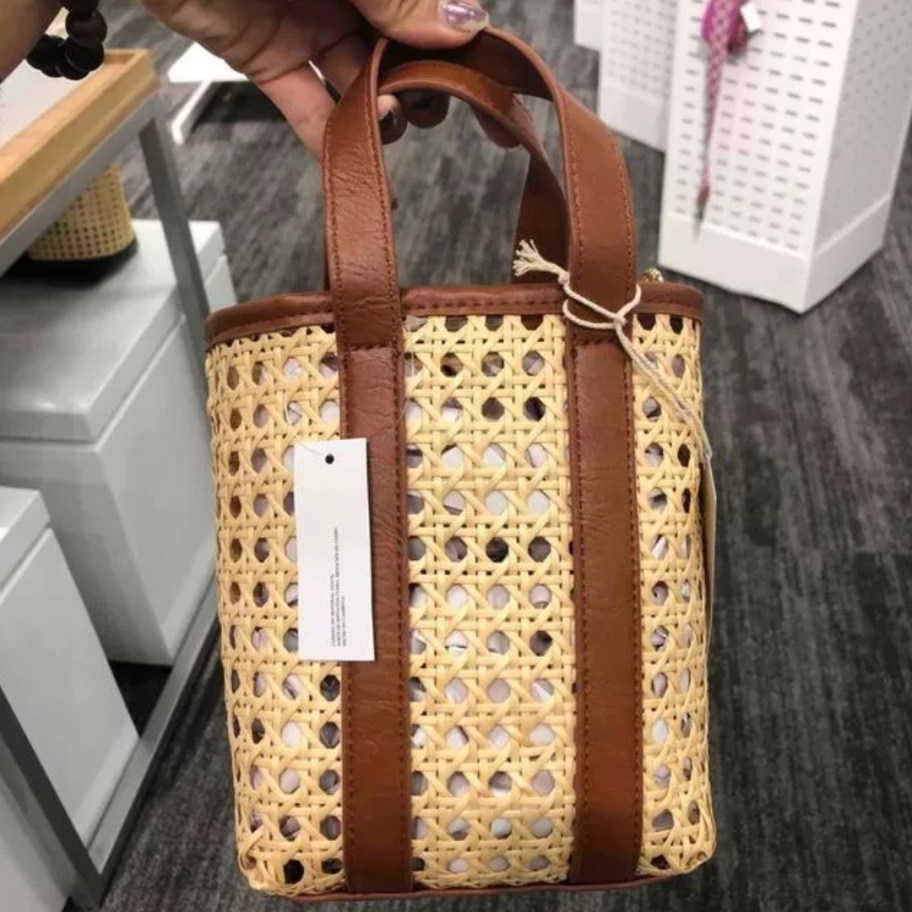 hand holding a small handbag with caning and brown straps and accents