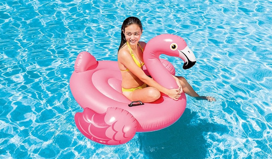 Girl sitting on an inflatable flamingo pool float in a pool