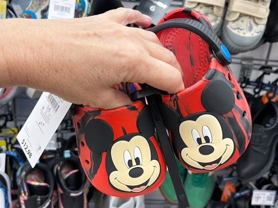 hand holding a pair of red and black mickey mouse clogs