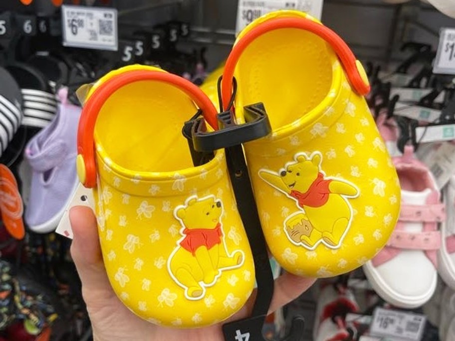 hand holding a pair of yellow Winnie the Pooh Baby Clogs