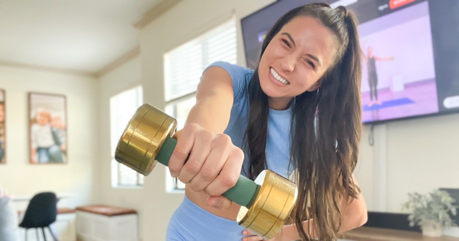 Woman holding weights in front of tv