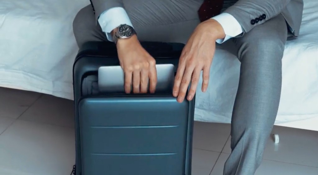 business man putting laptop into front pocket of away luggage alternatives