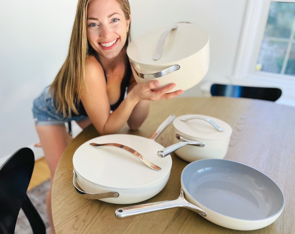 woman holding stock pot with various other caraway cookware pots and pans on table