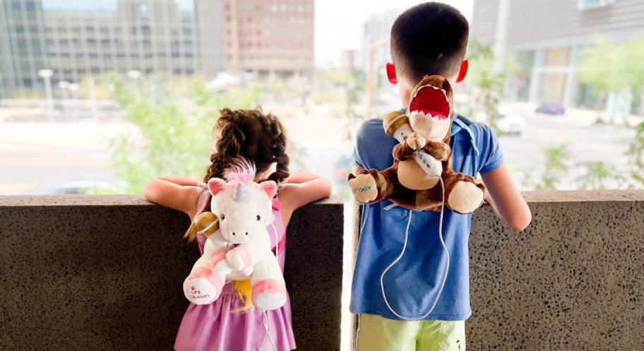 kids wearing unicorn and dinosaur backpacks looking at city