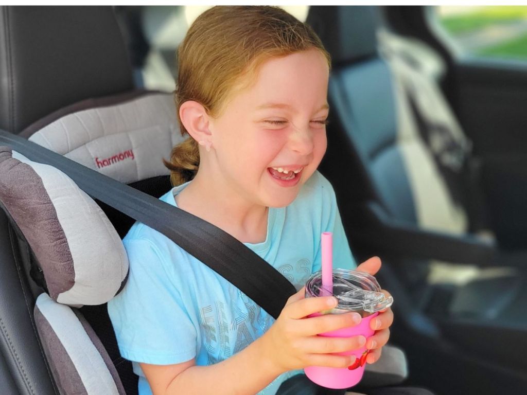 little girl in carseat holding cup with straw