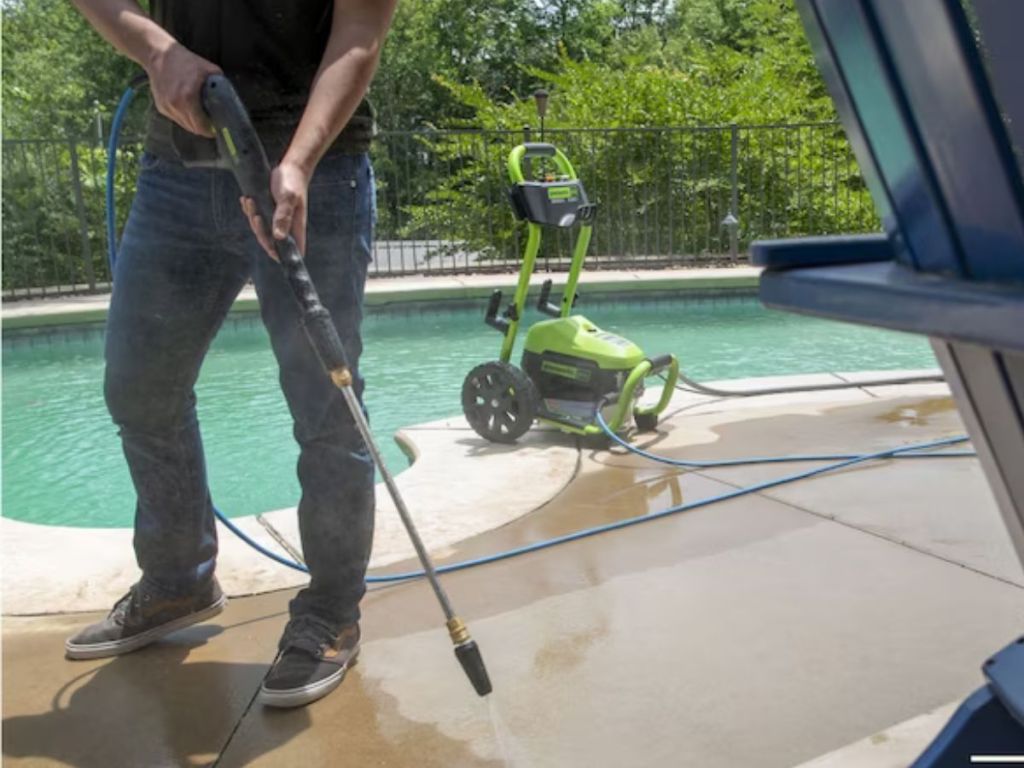 A man using a Greenworks Pressue Washer to clean around a pool