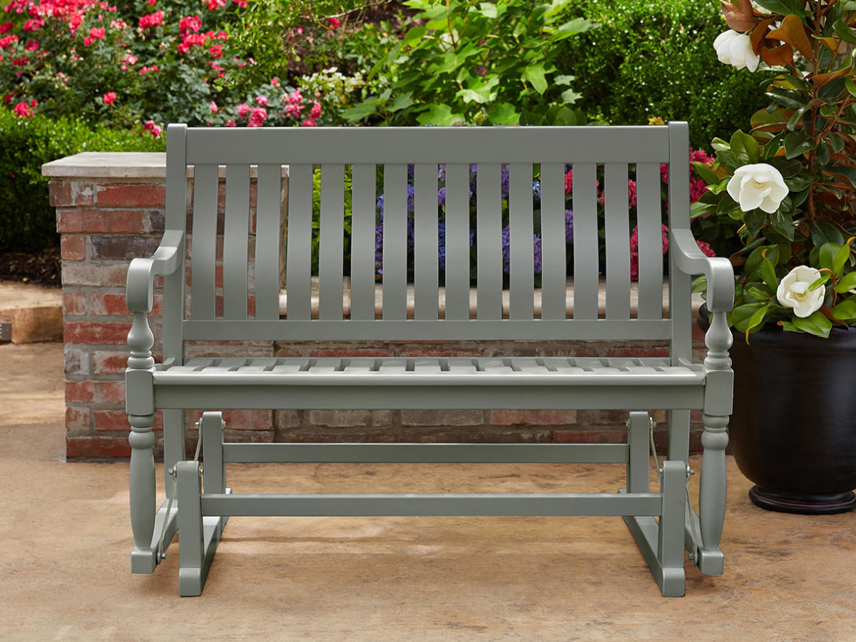 gray members mark glider bench outside in front of a brick divider wall