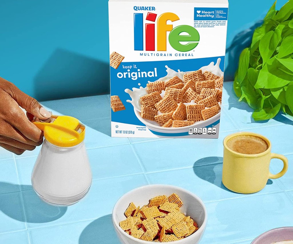 life cereal on a blue table with a bowl of cereal and a person holding a pitcher of milk