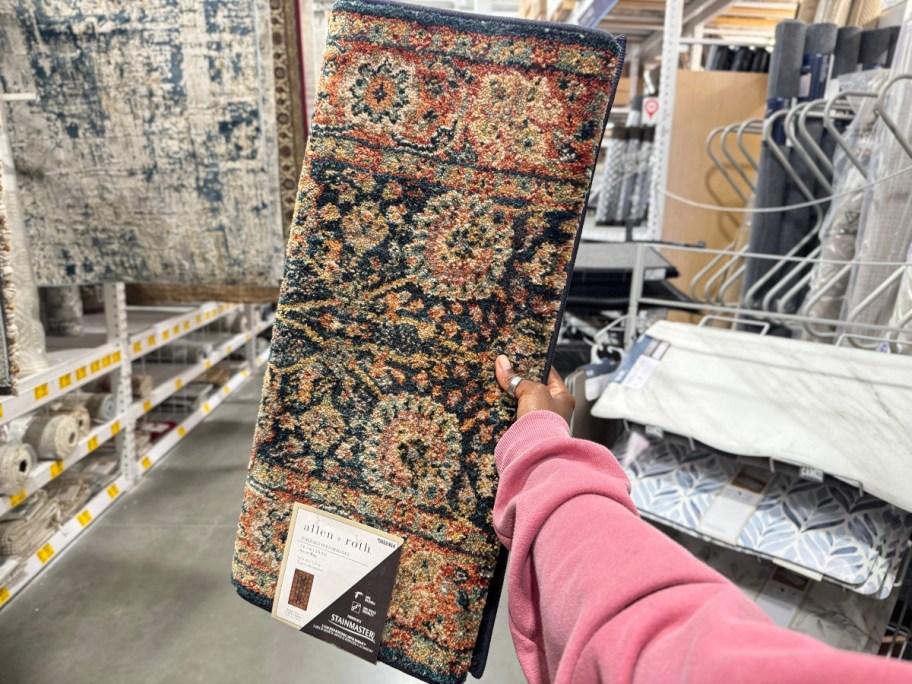 hand holding a runner rug with browns, greens, blacks