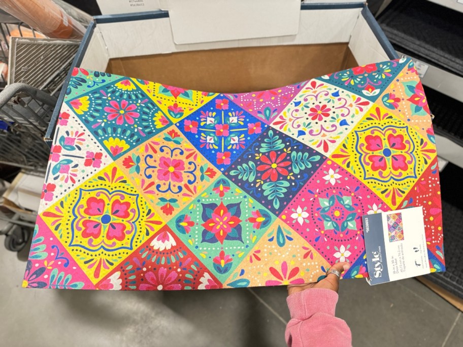 hand reaching for a colorful patchwork doormat with in a store display bin