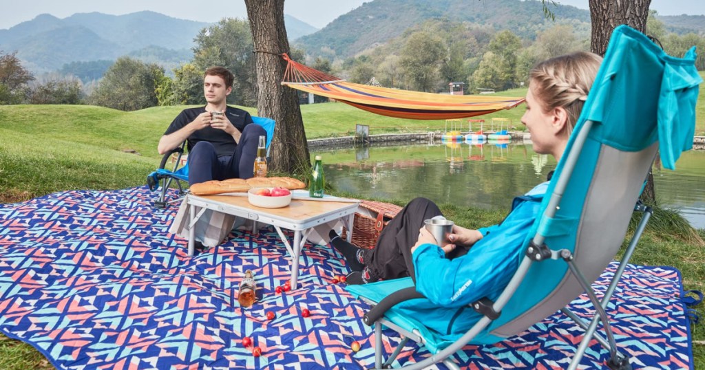 man and woman sitting in camping chairs on outdoor blanket in park