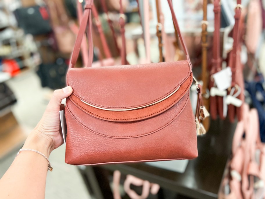 A woman holding a redish-brown purse in a store